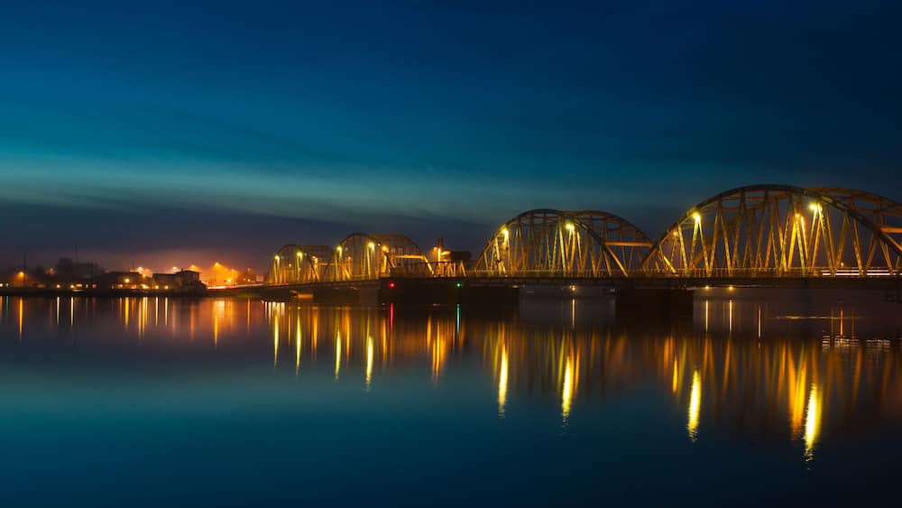 Ein Nachtblick auf eine Brücke, deren beleuchtete Lichter sich im Wasser spiegeln.