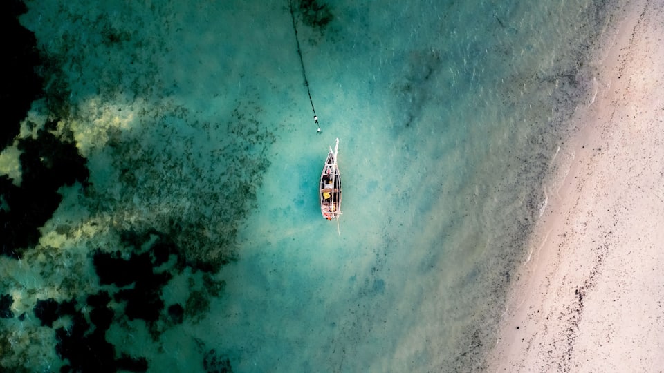 A small boat anchored near a sandy beach with clear turquoise water.