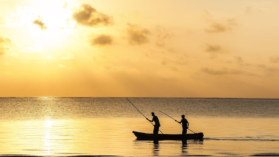 A sunset over a calm sea with two people fishing in a small boat.