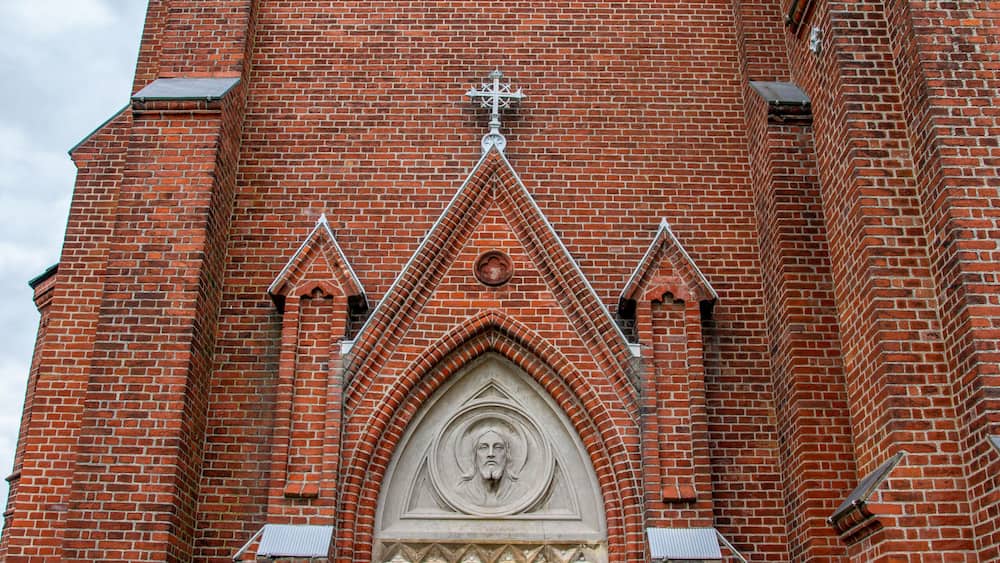 Eine rote Backsteinkirche mit einer großen Holztür, einer Uhr und einem Kruzifix obenauf.