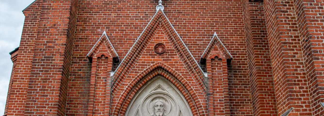 Una iglesia de ladrillo rojo con una puerta de madera grande, un reloj y una cruz en la parte superior.