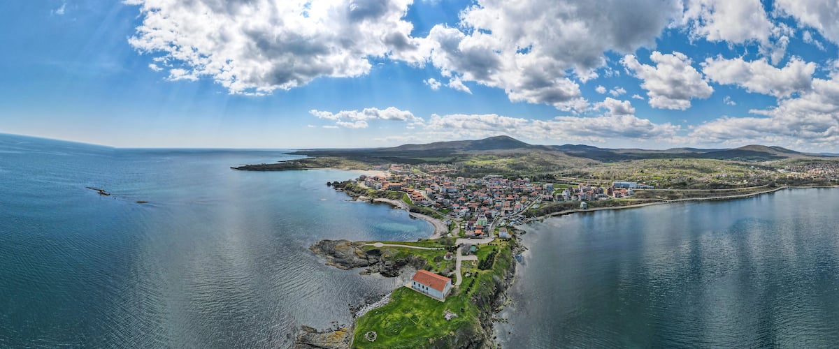 A coastal town with a bay, mountains in the background, and a clear sky.