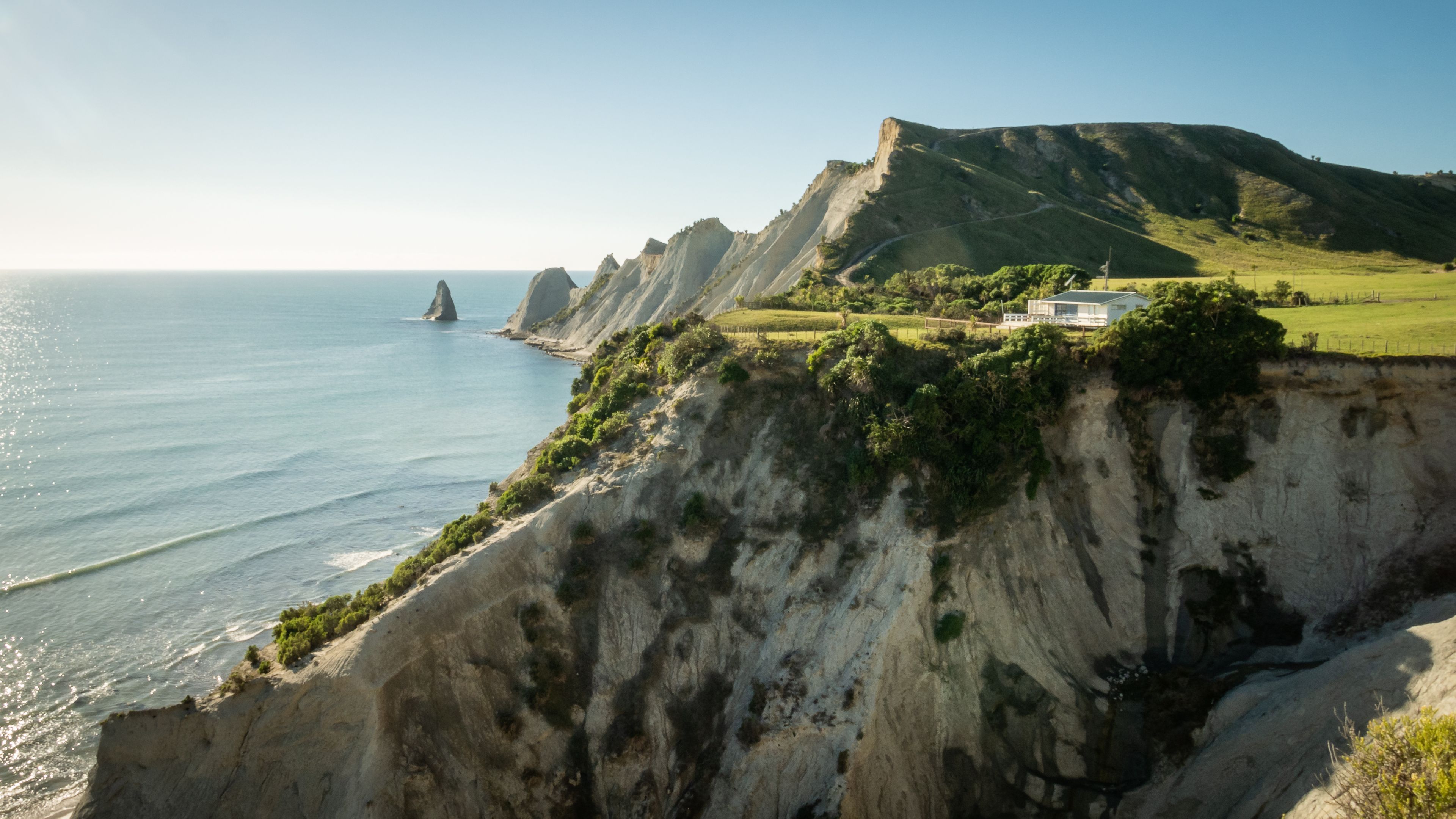 White house build on the cliff with cape and ocean in background. Shot made during cloudless sunny day on Cape Kidnappers Trail, New Zealand