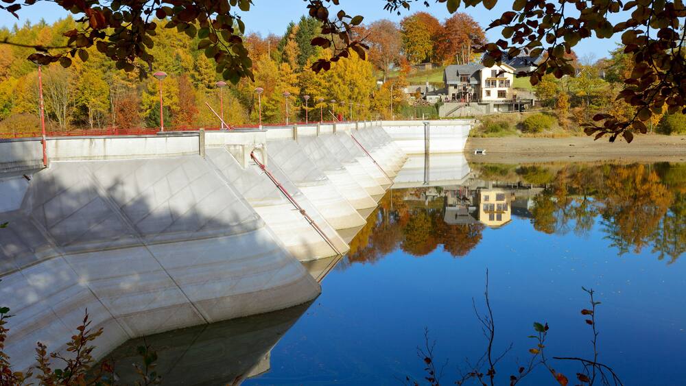 Un barrage en béton surplombant un lac paisible où se reflètent les arbres et les bâtiments.