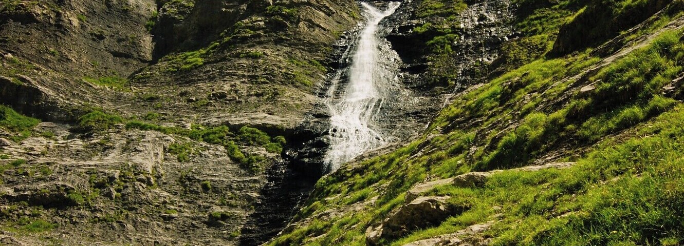 Una cascada se precipita por una ladera rocosa con abundante vegetación.