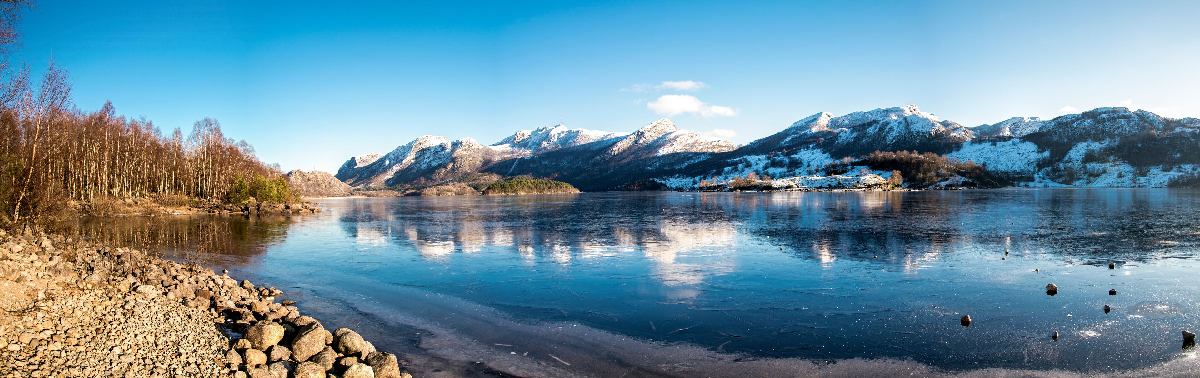 Panorama of nearly frozen Oltedalsvatnet lake and coastline with mountains peaks covered by snow during winter season, Gjesdal commune, Norway, February 2018