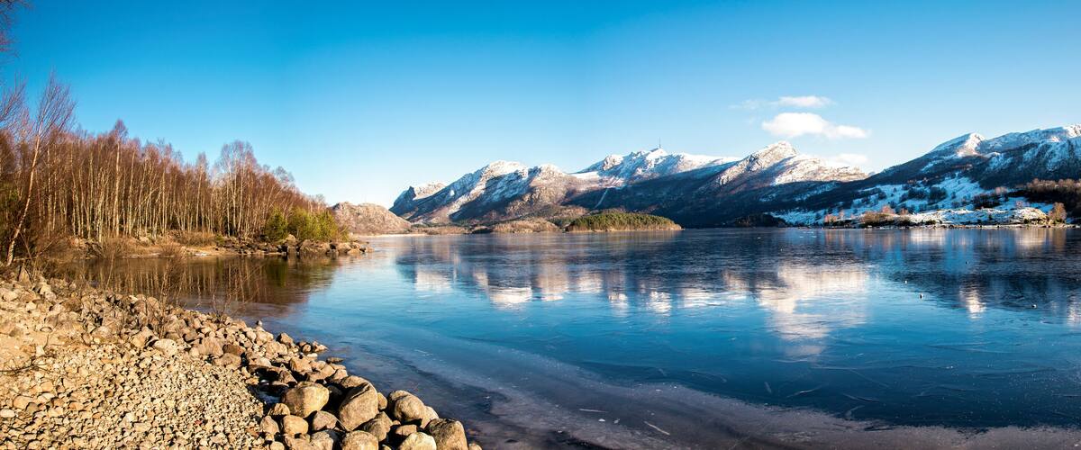 Panorama of nearly frozen Oltedalsvatnet lake and coastline with mountains peaks covered by snow during winter season, Gjesdal commune, Norway, February 2018