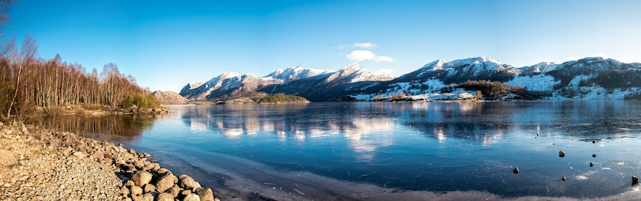 Panorama of nearly frozen Oltedalsvatnet lake and coastline with mountains peaks covered by snow during winter season, Gjesdal commune, Norway, February 2018