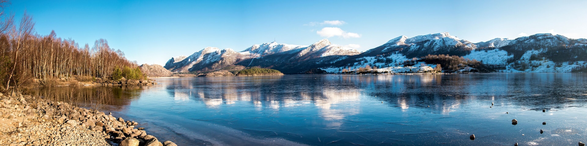 Panorama of nearly frozen Oltedalsvatnet lake and coastline with mountains peaks covered by snow during winter season, Gjesdal commune, Norway, February 2018