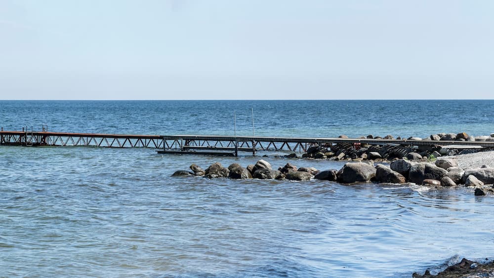 A pier extending into calm waters, a rocky shoreline, and a small boat with a red cover.