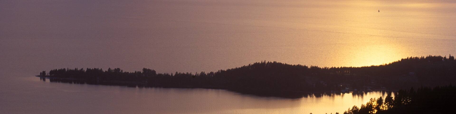 A calm lake at sunset with mountains in the background and a small island in the foreground.