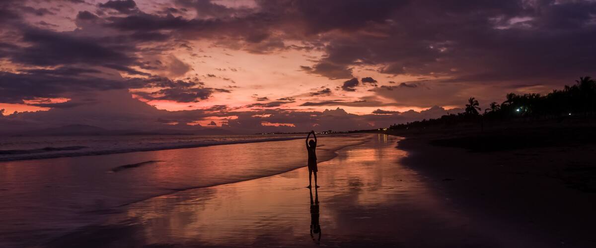 A beach at sunset with a person standing in the sand.