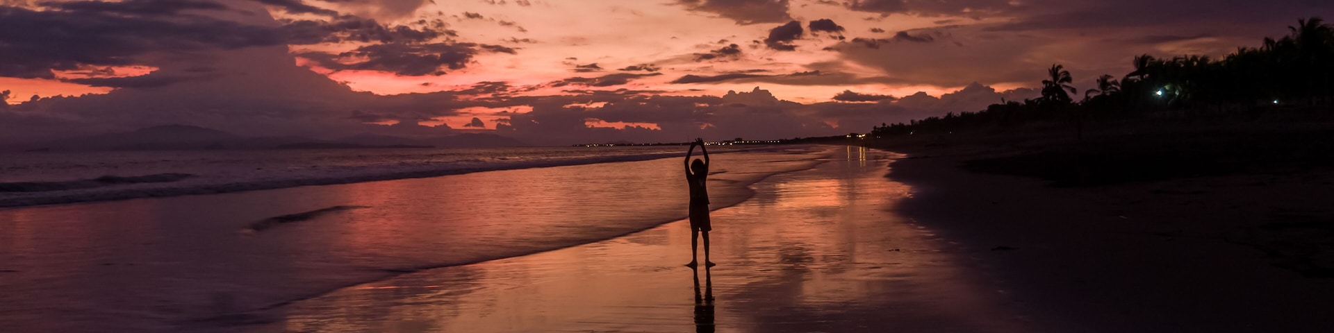 A beach at sunset with a person standing in the sand.