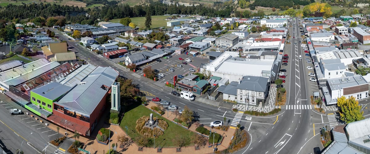 A town with a central road, surrounding buildings, and hills in the background.