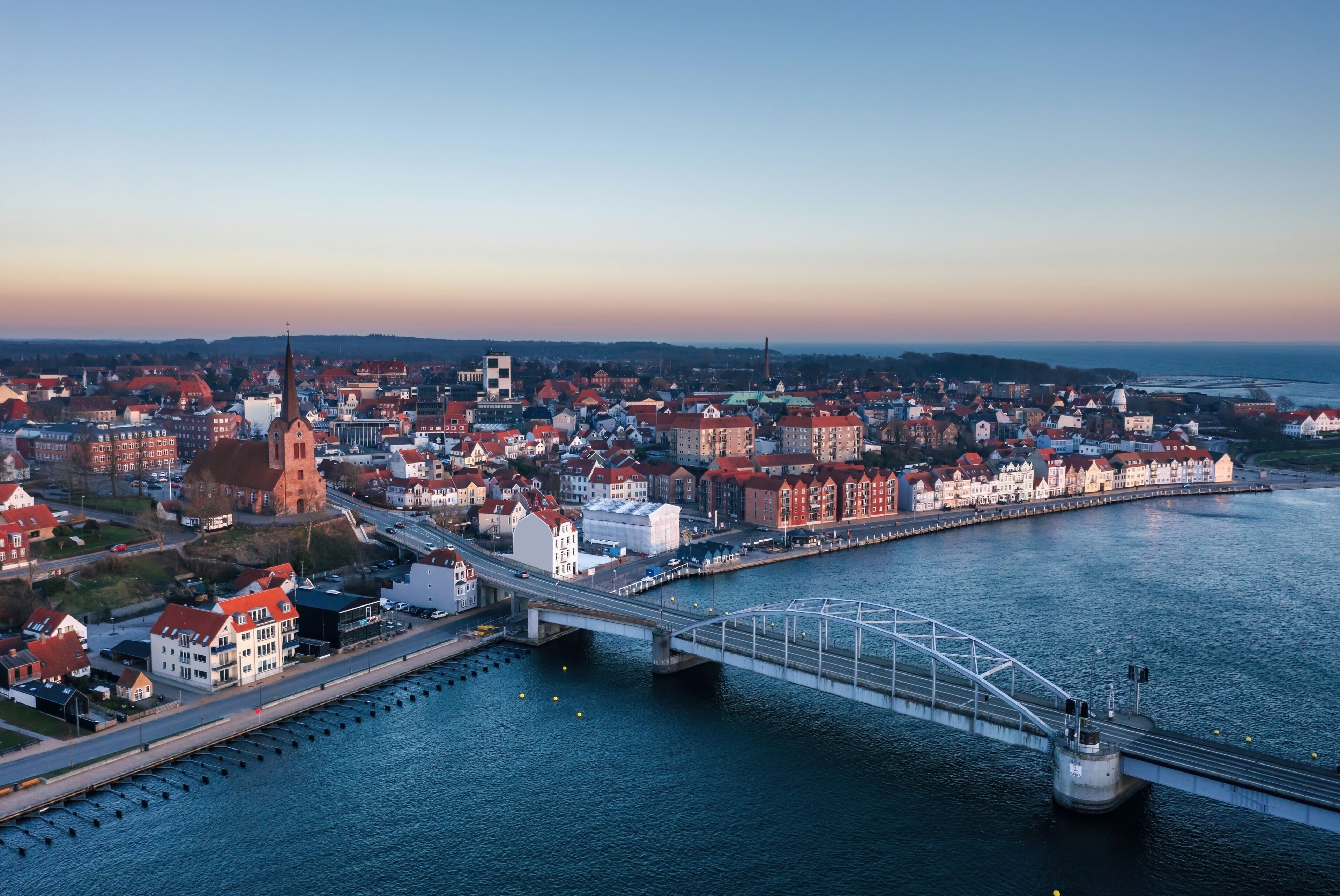 A coastal cityscape with a prominent church, a bridge, and a waterfront promenade.