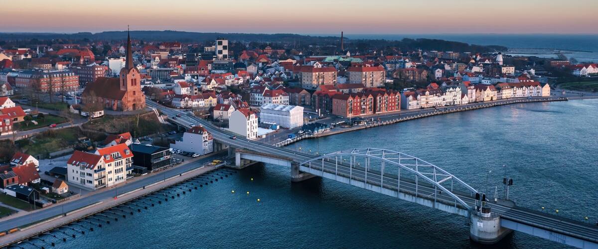 A coastal cityscape with a prominent church, a bridge, and a waterfront promenade.