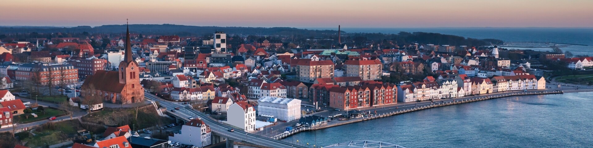 A coastal cityscape with a prominent church, a bridge, and a waterfront promenade.