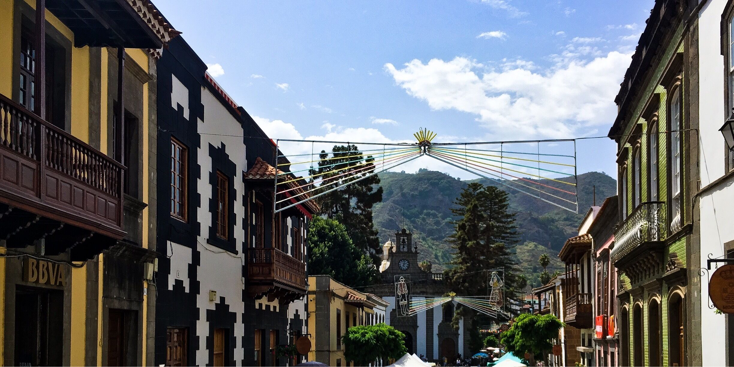 A street with buildings, a clock tower, and a mountain in the background.