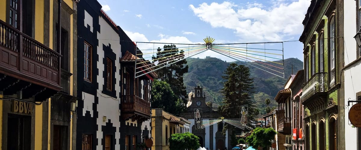 A street with buildings, a clock tower, and a mountain in the background.