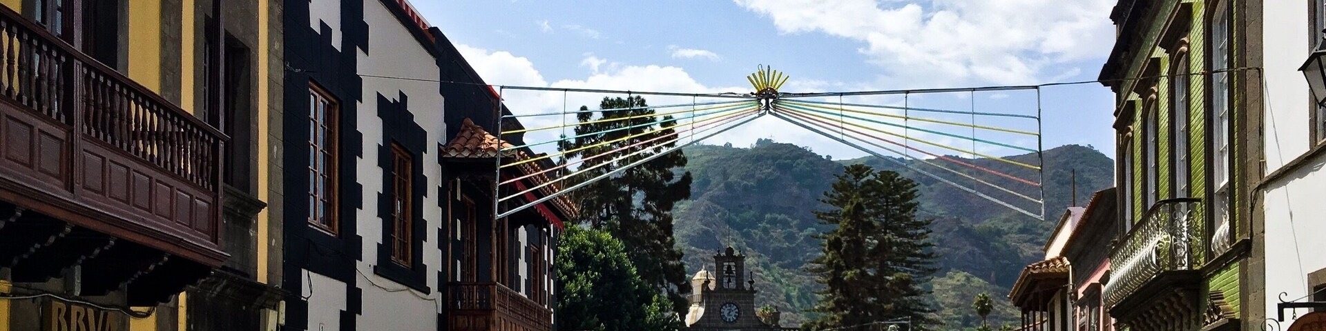 A street with buildings, a clock tower, and a mountain in the background.