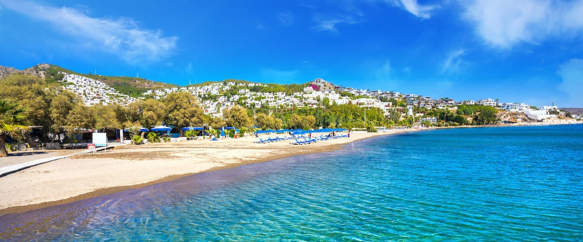 A clear blue sea, a sandy beach, and a hillside with buildings.