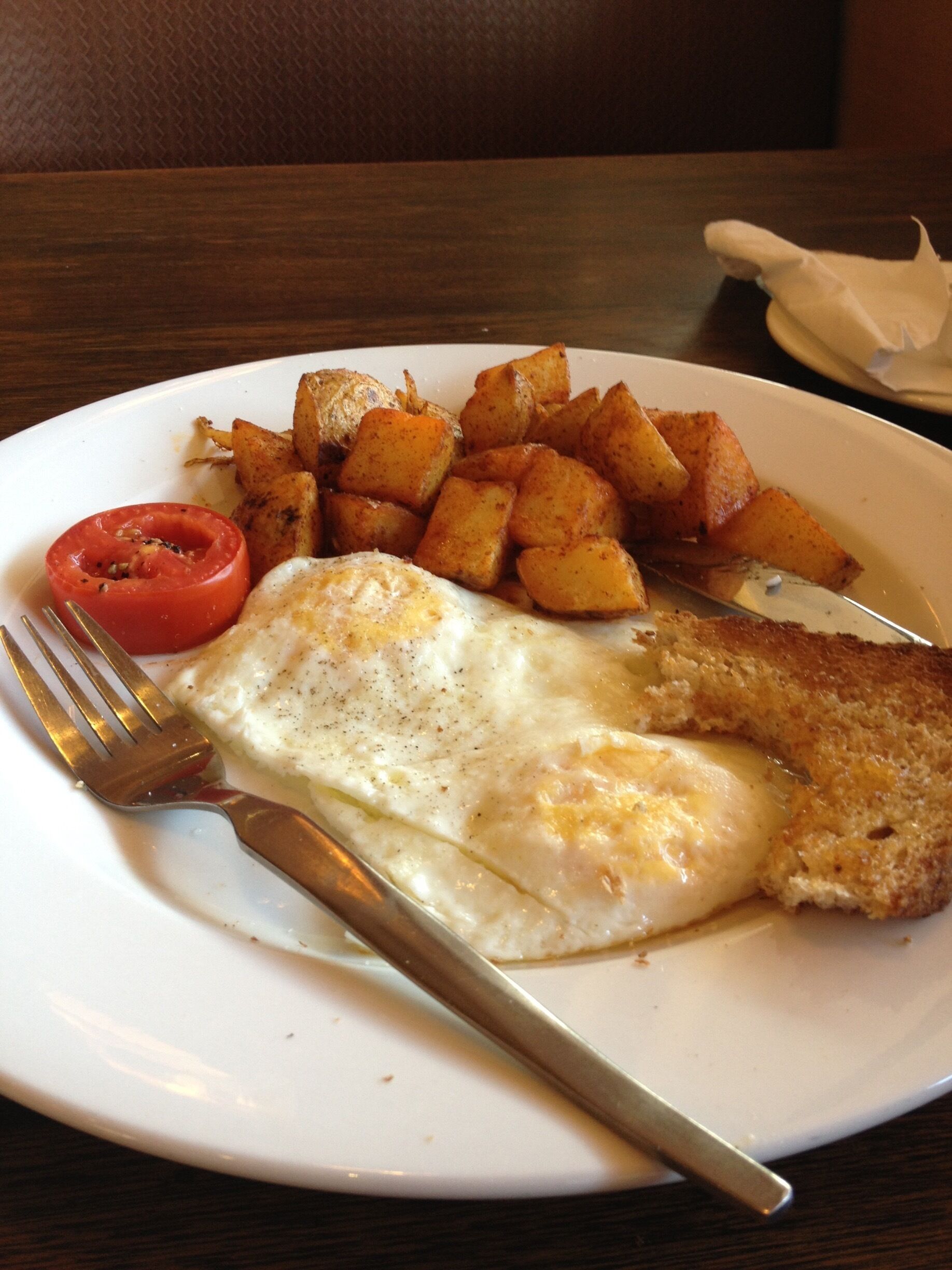 A plate with a fried egg, hash browns, and a slice of tomato.