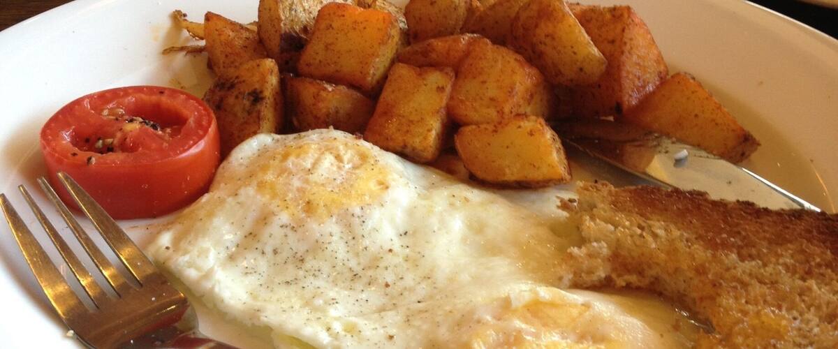 A plate with a fried egg, hash browns, and a slice of tomato.
