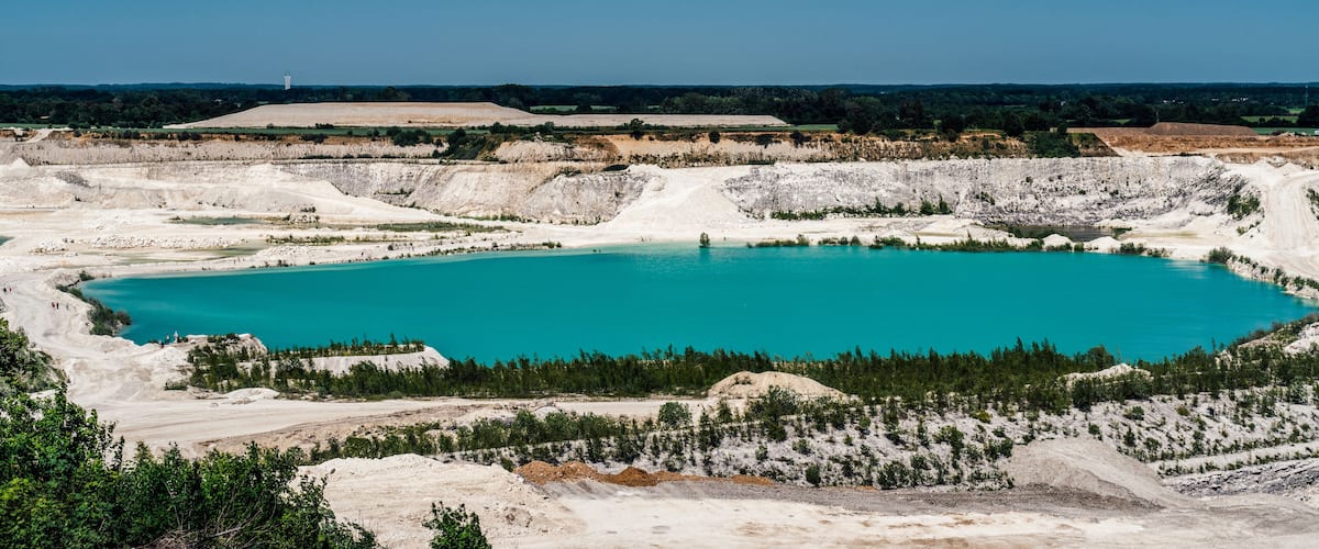 A large turquoise lake surrounded by white rock formations and sparse vegetation.