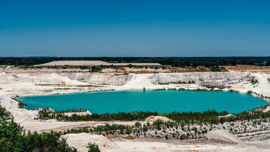 A large turquoise lake surrounded by white rock formations and sparse vegetation.