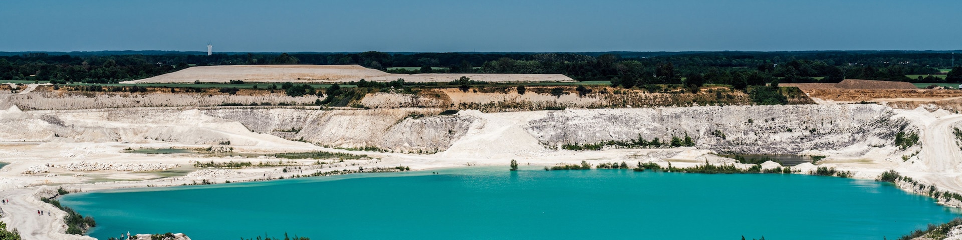 A large turquoise lake surrounded by white rock formations and sparse vegetation.