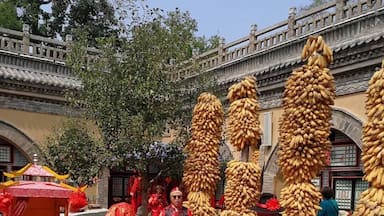 A traditional ceremony with participants in red attire, a red carpet, and a backdrop of a stone building with arches.