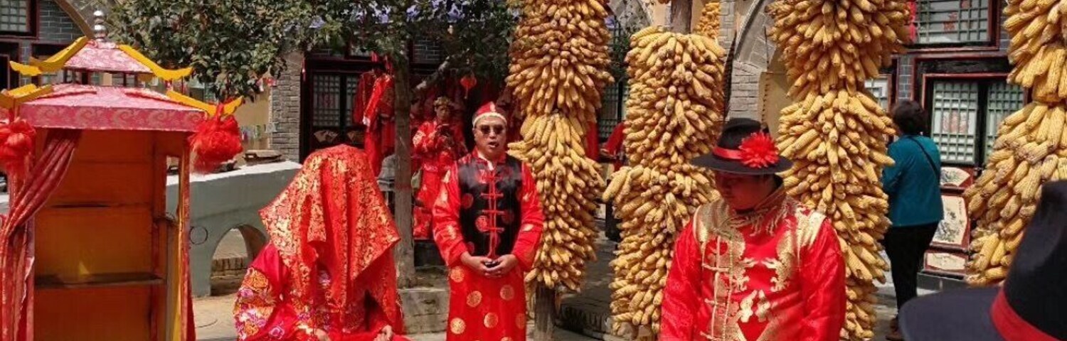 A traditional ceremony with participants in red attire, a red carpet, and a backdrop of a stone building with arches.