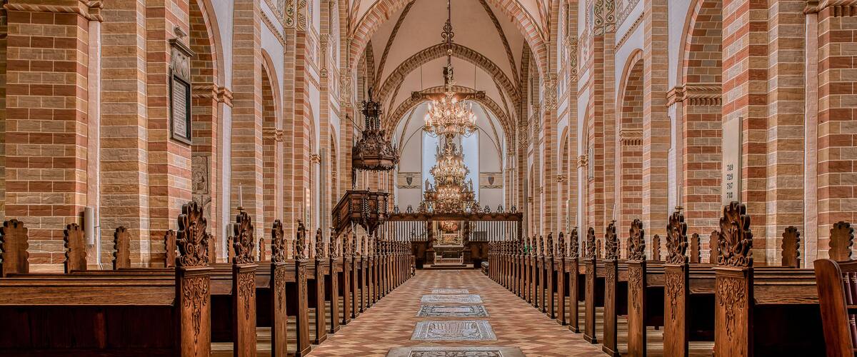 A church interior with a long aisle, wooden pews, and a central altar.