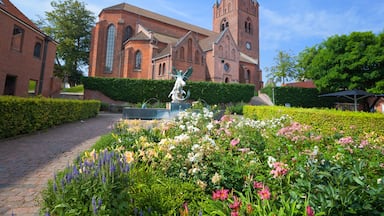 A historic church with a tall spire, surrounded by a well-maintained garden with various flowers and a statue.