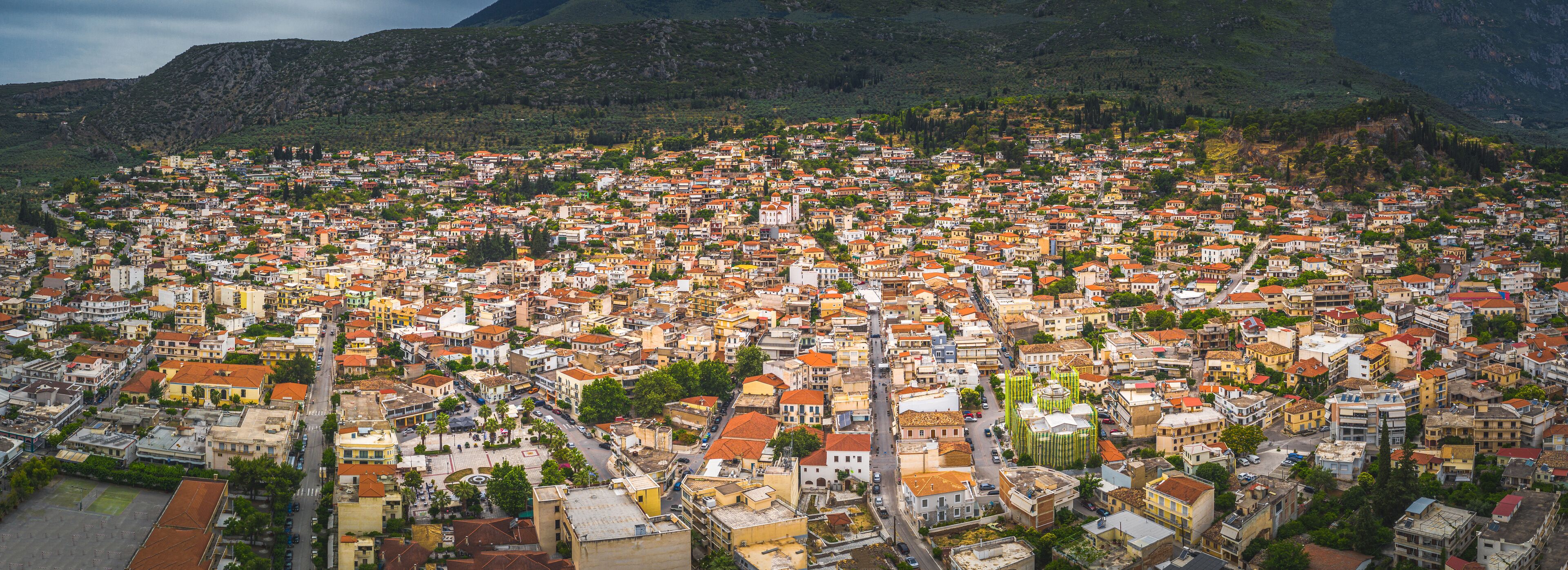 A densely packed town with red-roofed buildings, surrounded by green hills.