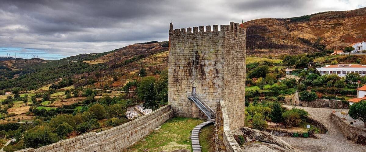 A medieval castle with a stone wall and a winding path leading to a tower.