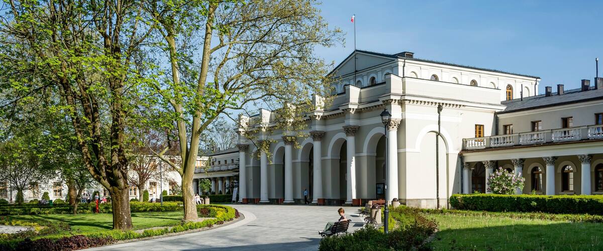 A grand building with classical architecture, a well-maintained garden, and a clear blue sky.
