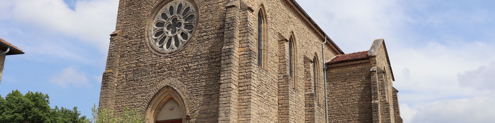 Igreja de pedra com uma grande janela circular e uma cruz no topo.