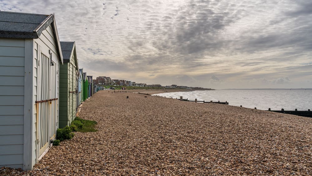 A pebble beach with buildings on the left and a cloudy sky.