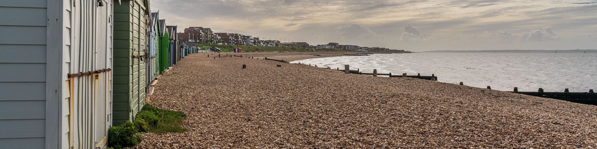 A pebble beach with buildings on the left and a cloudy sky.
