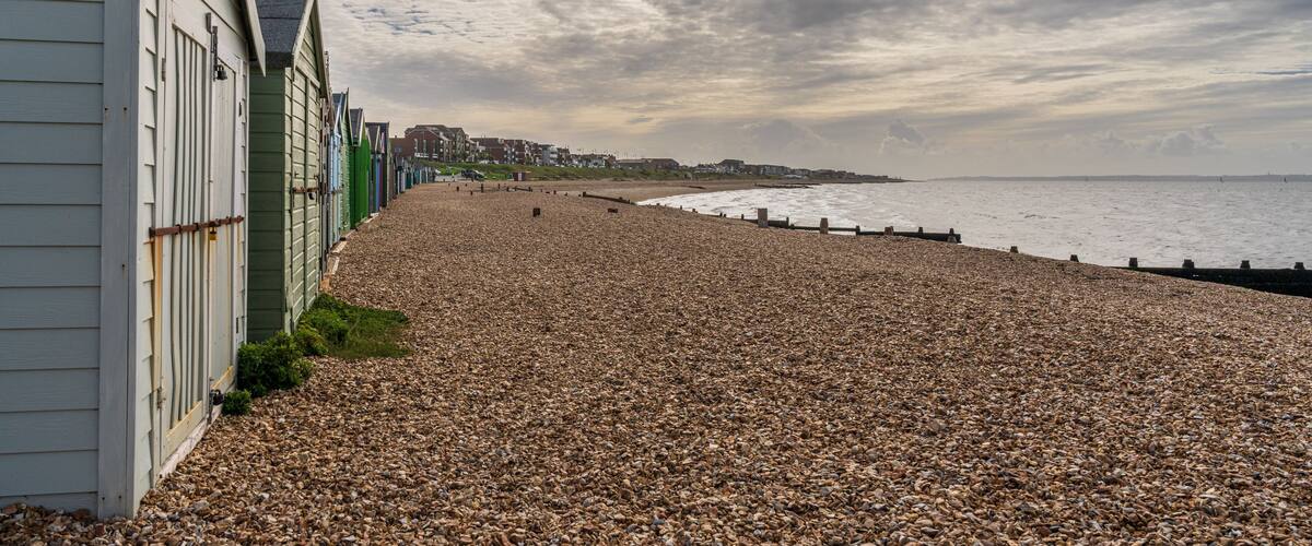 A pebble beach with buildings on the left and a cloudy sky.