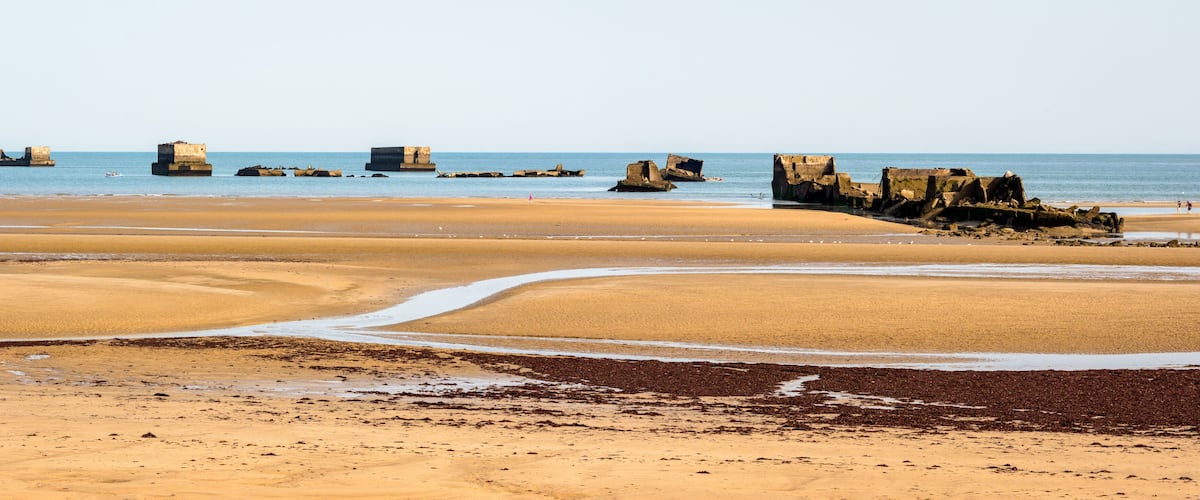 A sandy beach with large rock formations in the water.