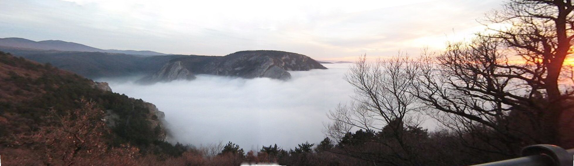 Paisaje montañoso con un valle cubierto de niebla, cielo despejado y un atardecer.