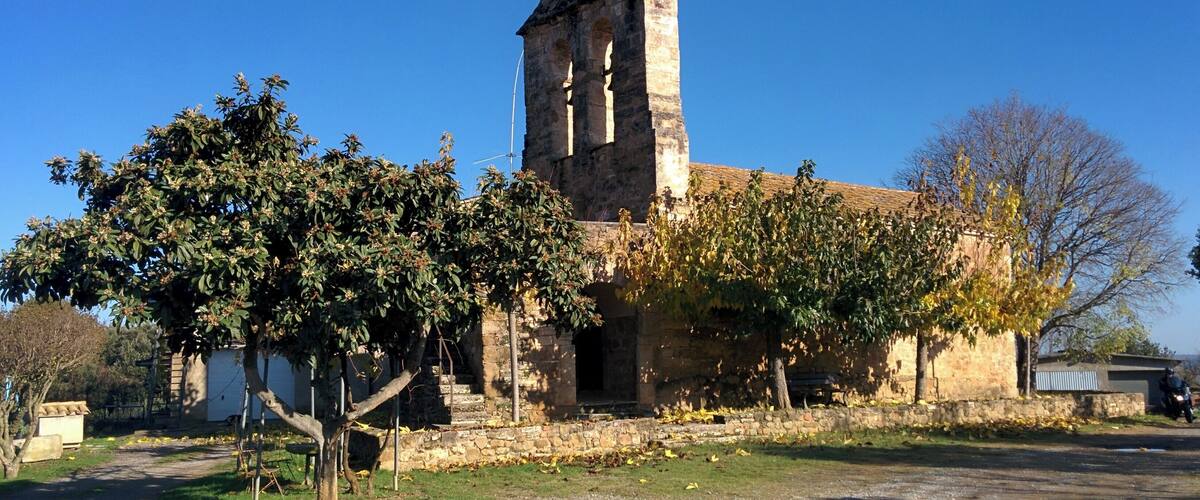 An old stone church with a bell tower, surrounded by trees and a gravel path.