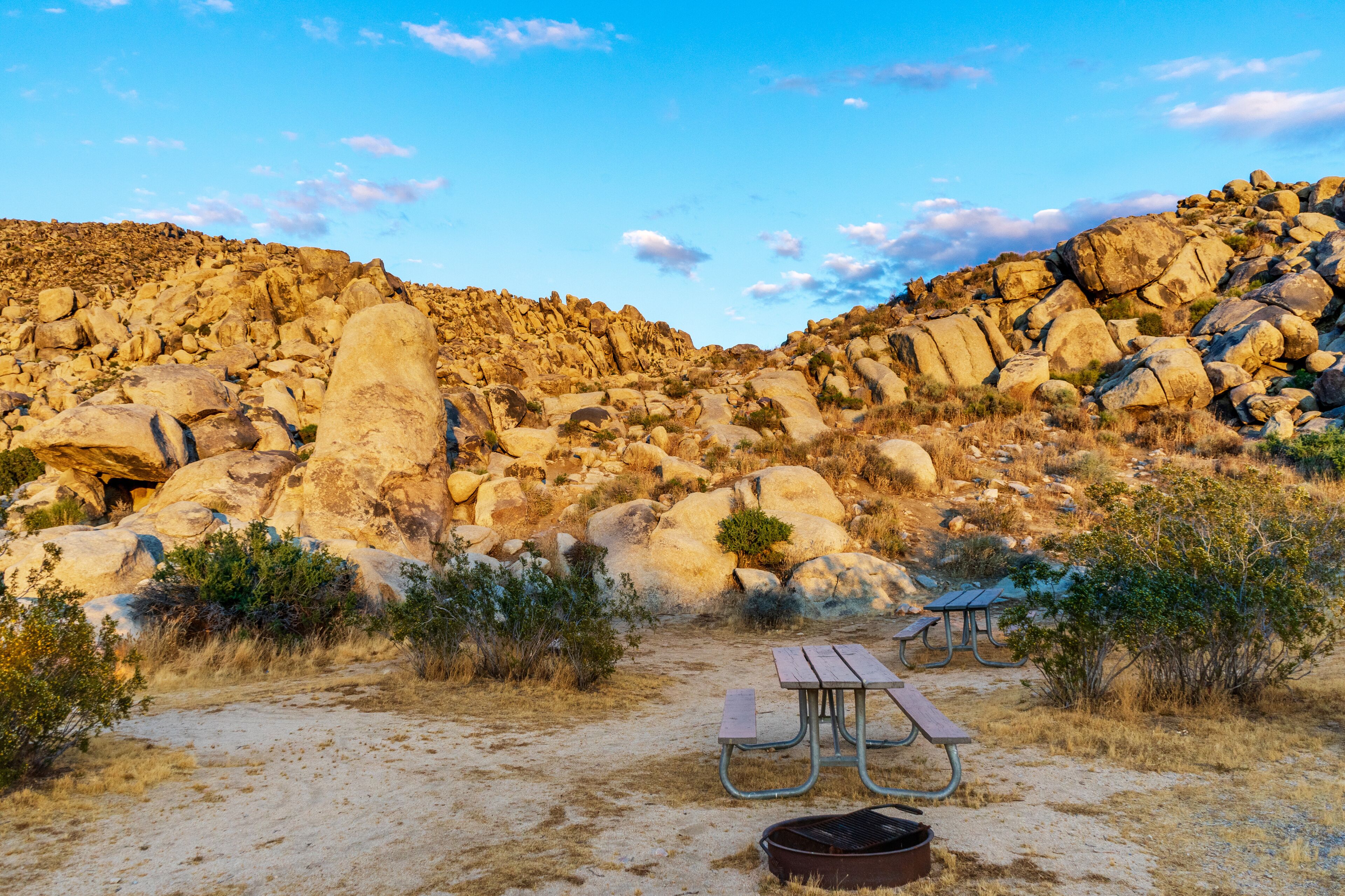 A rocky desert landscape with a picnic table and grill.