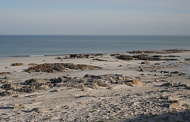 Una playa rocosa con grandes rocas dispersas y agua tranquila al fondo.