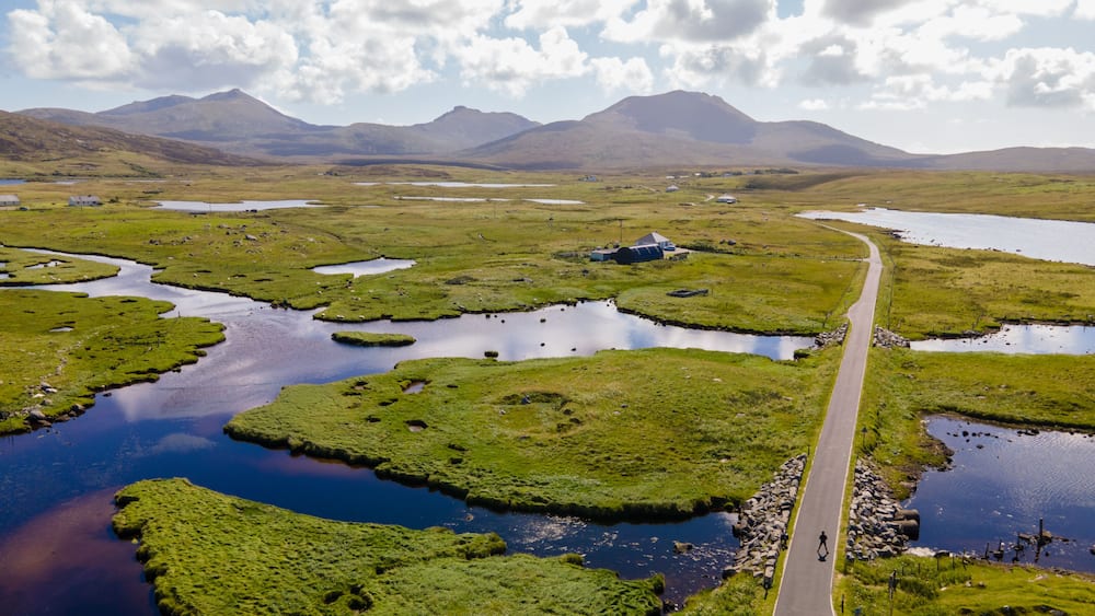 A landscape with a winding road, multiple small lakes, and distant mountains under a partly cloudy sky.