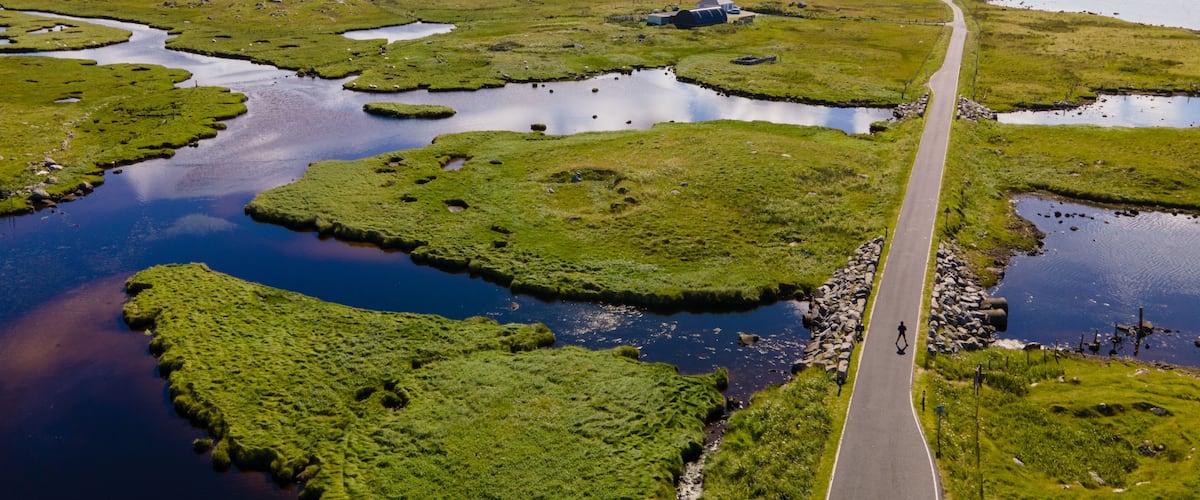 Paisagem com estrada sinuosa, vários lagos pequenos e montanhas ao longe sob um céu parcialmente nublado.