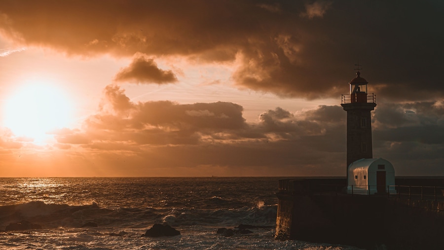 Un faro junto al mar durante el atardecer con olas rompiendo contra las rocas.