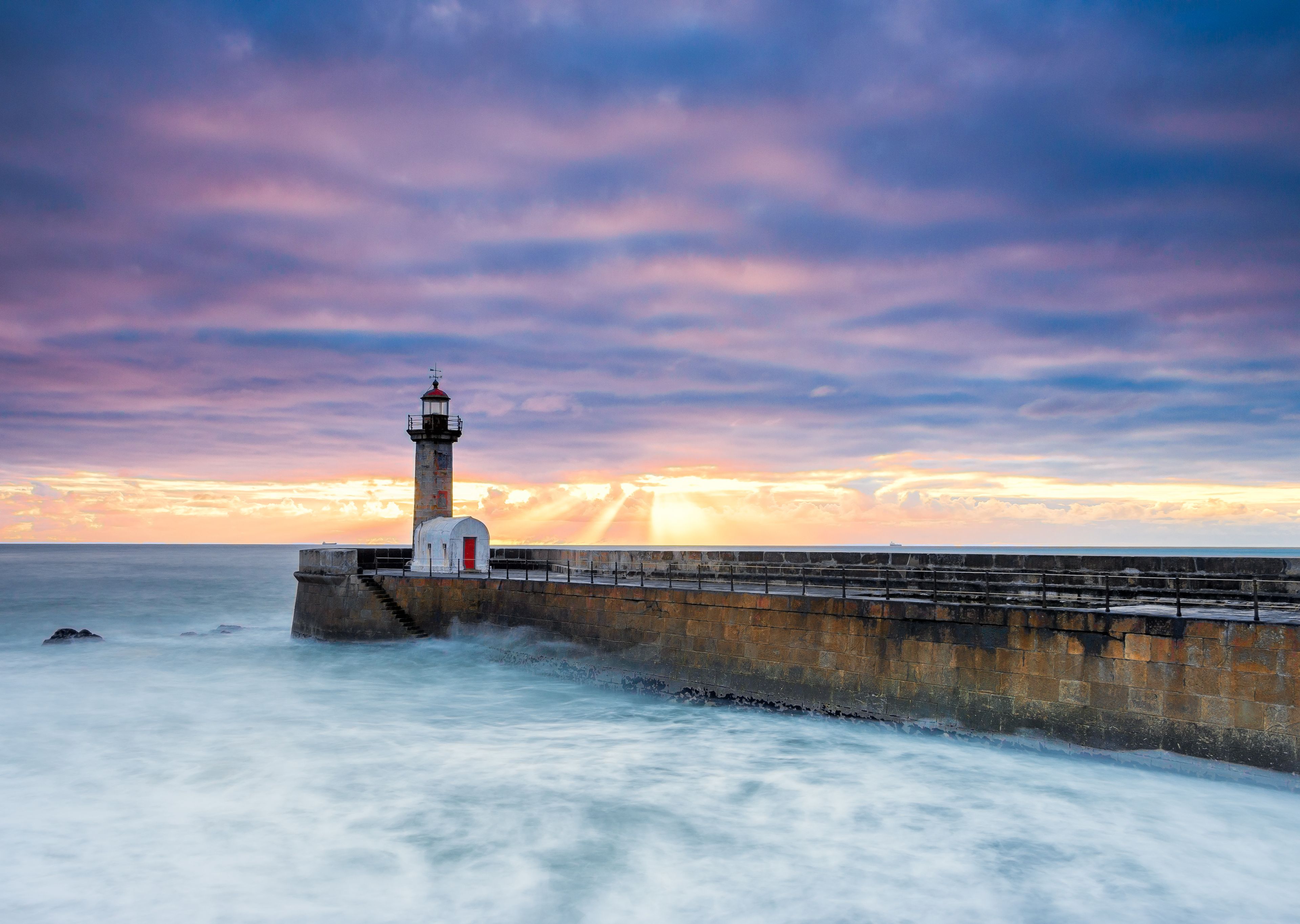 A lighthouse by the sea with a sunset in the background.